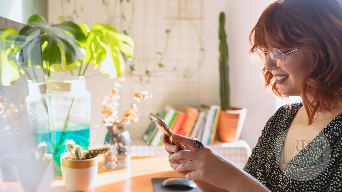 Psicóloga sonriente consultando el móvil en su despacho luminoso, con plantas y libros al fondo: la agenda de la consulta sincronizada con Google Calendar