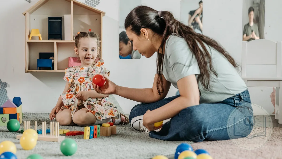 Terapeuta de atención temprana sentada en el suelo juega con una niña pequeña con pelotas y bloques en una sala de estimulación
