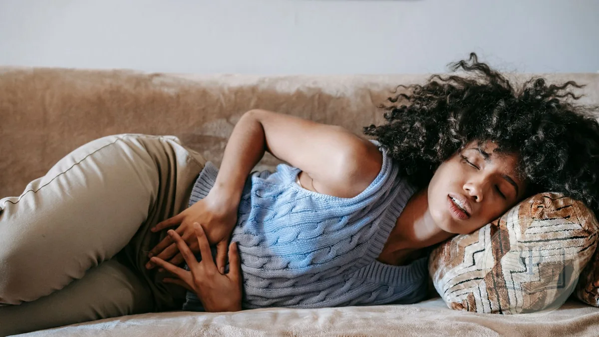 Mujer tumbada en el sofá con las manos en el abdomen por un dolor persistente sin causa médica